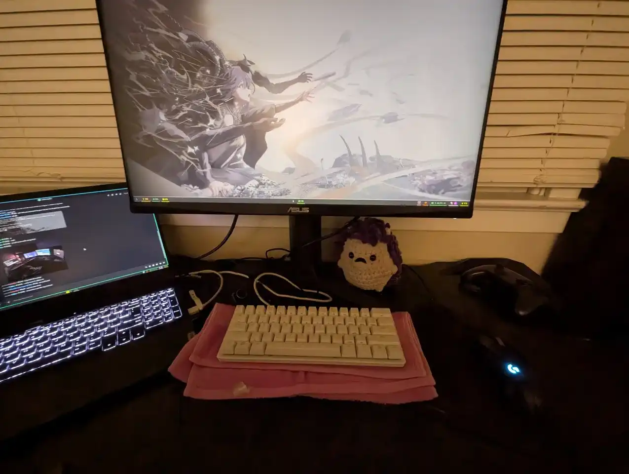 
        Picture of my setup with a black desk, laptop on the left, monitor in the middle, with a white keyboard and a black mouse. There is also a purple hedgehog and a pink towel under the keyboard to reduce noise.